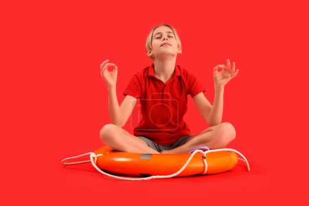 Salvavidas niño pequeño con boya anillo meditando sobre fondo rojo