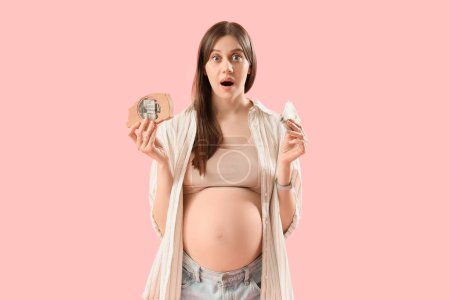 Shocked young pregnant woman with piggy bank and money on pink background. Maternal Benefit concept