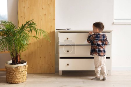 Petit garçon ouvrant des tiroirs à la maison, vue de derrière. Enfant en danger