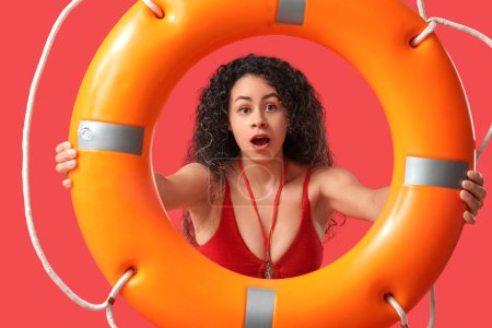 Photo for Beautiful young shocked African-American female lifeguard with ring buoy on red background - Royalty Free Image