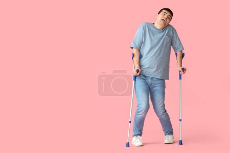 Junger Mann mit Krücken auf rosa Hintergrund. Nationaler Monat des Bewusstseins für Zerebralparese