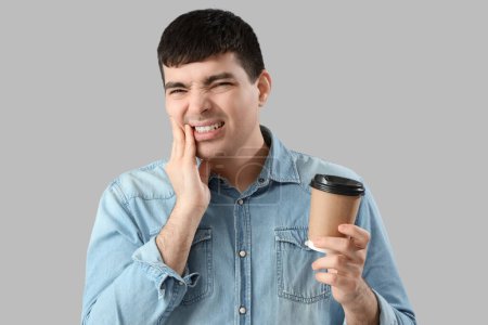 Young man with coffee cup suffering from toothache on light background, closeup