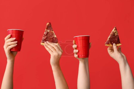 Téléchargez les photos : De nombreuses mains tenant de savoureuses tranches de pizza et des tasses à usage unique sur fond rouge - en image libre de droit