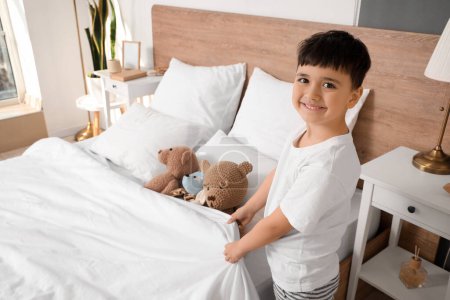 Photo for Cute happy little boy with toys making bed in bedroom - Royalty Free Image