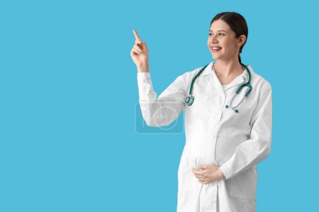 Téléchargez les photos : Jeune médecin enceinte pointant quelque chose sur fond bleu - en image libre de droit
