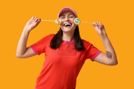 Foto de Mujer joven feliz con piruletas dulces sobre fondo amarillo - Imagen libre de derechos