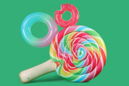 Inflatable rings and swimming mattress in shape of candy on green background