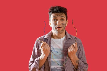 Electrocuted young man with burnt face and wires on red background