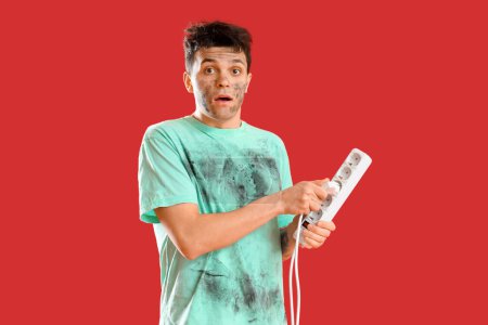 Electrocuted young man with burnt face and extension cord on red background