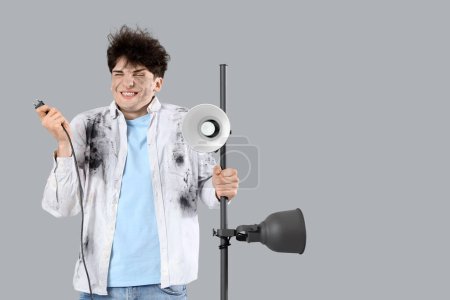 Electrocuted young man with burnt face and lamp on light background