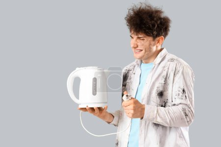 Electrocuted young man with burnt face and electric kettle on light background