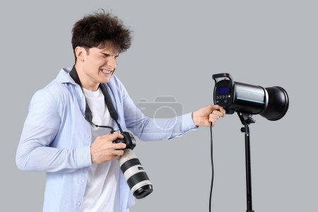 Electrocuted male photographer with burnt face and camera inserting plug on light background