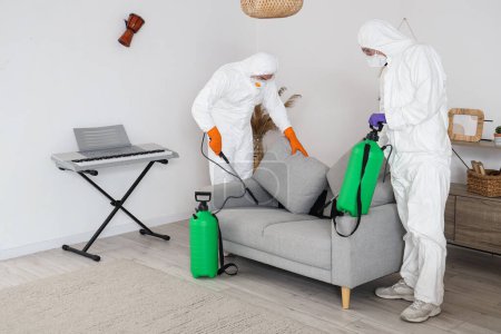 Foto de Trabajadores masculinos desinfectando sofá en la habitación - Imagen libre de derechos