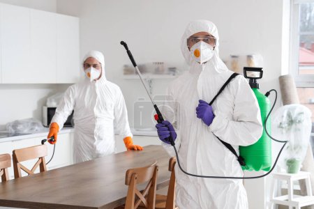 Foto de Trabajadores masculinos en trajes de materiales peligrosos desinfectando la cocina - Imagen libre de derechos