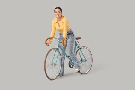 Beautiful young woman riding bicycle on grey background