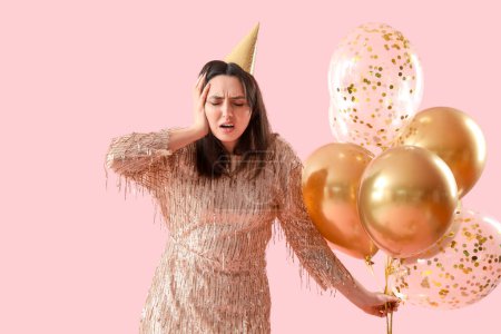 Téléchargez les photos : Jeune femme avec gueule de bois et ballons après la fête d'anniversaire sur fond rose - en image libre de droit