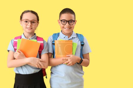 Photo for Happy little pupils with backpacks and notebooks on yellow background - Royalty Free Image