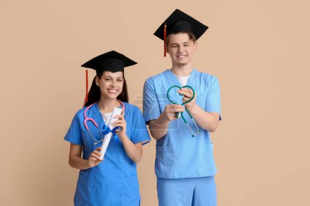 Photo for Happy medical graduate couple with diplomas and stethoscopes on beige background - Royalty Free Image
