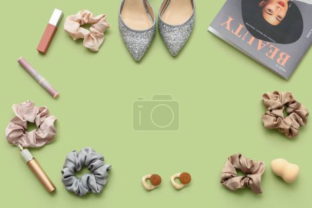 Frame made of trendy silk scrunchies with cosmetics, shoes and magazine on green background