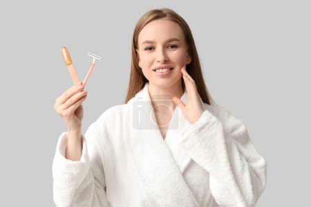 Schöne junge glückliche Frau hält Rasiermesser und Spachtel mit Zuckerpaste auf grauem Hintergrund