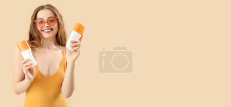 Beautiful young woman with sunscreen creams on beige background with space for text