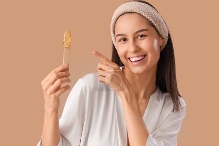Belle jeune femme heureuse pointant vers la spatule avec de la pâte à sucre sur fond brun