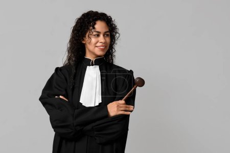 Photo for Beautiful young happy African-American female judge with gavel on grey background - Royalty Free Image