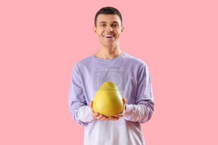 Young man with pomelo on pink background