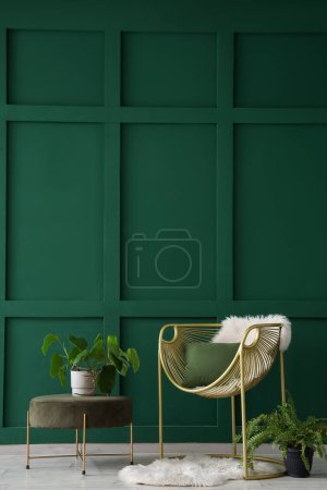 Innenraum des Wohnzimmers mit Sessel, Kissen und Zimmerpflanzen in der Nähe der grünen Wand