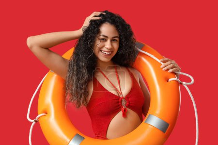 Photo for Beautiful young happy African-American female lifeguard with ring buoy on red background - Royalty Free Image