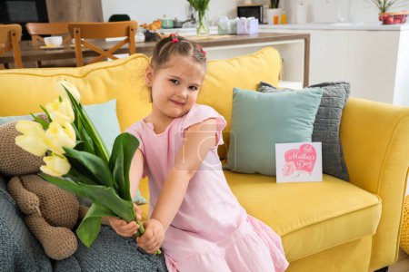 Téléchargez les photos : Jolie petite fille assise sur un canapé avec un bouquet de tulipes à la maison. Fête des Mères - en image libre de droit