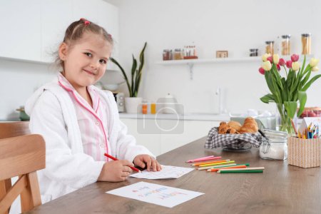 Téléchargez les photos : Mignonne petite fille dessin carte de voeux à la fête des mères à table dans la cuisine - en image libre de droit