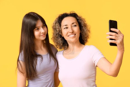 Schöne reife Frau mit ihrer Teenager-Tochter beim Selfie auf gelbem Hintergrund. Muttertag