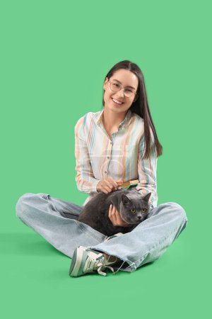 Téléchargez les photos : Jeune femme brossant mignon British Shorthair chat sur fond vert - en image libre de droit