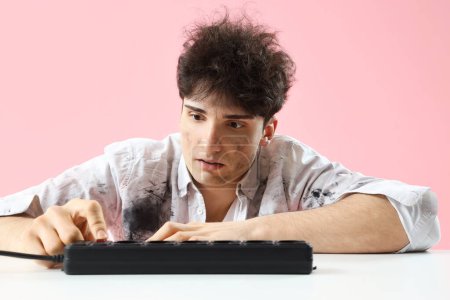 Electrocuted young man with burnt face and extension cord at table on pink background, closeup