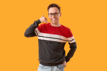 Cool young man showing "call me" gesture on yellow background