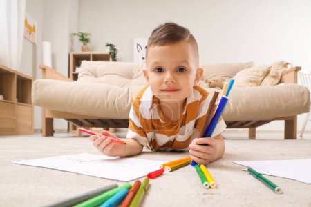 Cute little boy drawing with felt-tip pens on floor at home