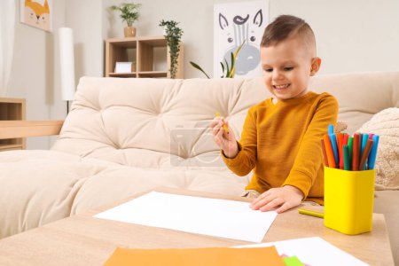 Cute little boy drawing with felt-tip pens on table at home
