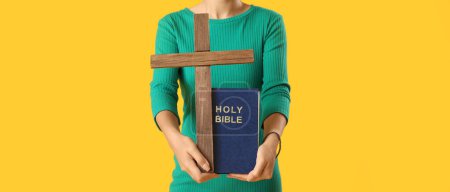 Foto de Mujer joven sosteniendo la cruz y la Biblia sobre fondo amarillo - Imagen libre de derechos