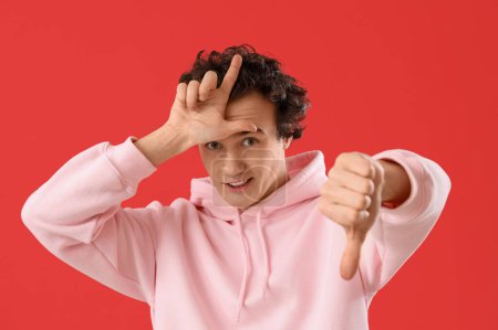 Young man showing loser gesture on red background