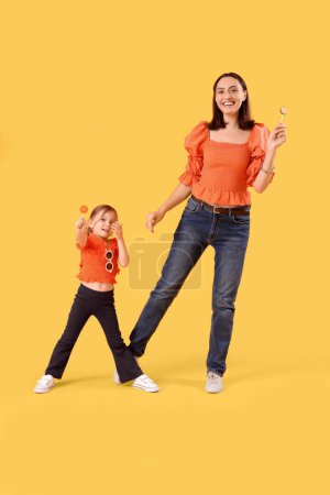 Foto de Hermosa madre y su linda hijita con piruletas dulces sobre fondo amarillo - Imagen libre de derechos