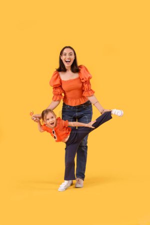 Foto de Hermosa madre y su linda hija pequeña con piruletas dulces que se divierten en el fondo amarillo - Imagen libre de derechos