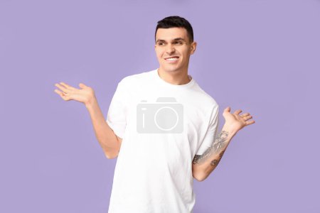 Téléchargez les photos : Beau jeune homme honteux haussant les épaules sur fond lilas - en image libre de droit