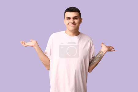 Photo for Handsome ashamed young man shrugging on lilac background - Royalty Free Image