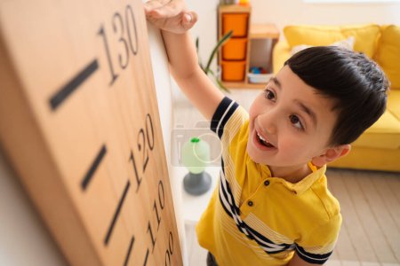 Cute little boy measuring height near wooden stadiometer at home, closeup