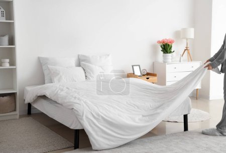 Photo for Woman making bed in modern bedroom - Royalty Free Image