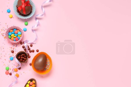 Foto de Tazas de papel con chocolate dulce Huevos de Pascua y caramelos sobre fondo rosa - Imagen libre de derechos
