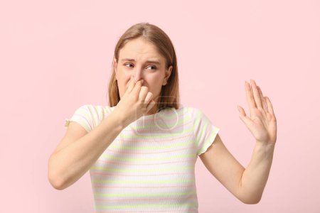 Young woman feeling bad smell on pink background