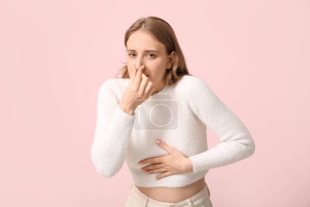 Young woman feeling disgusting smell on pink background