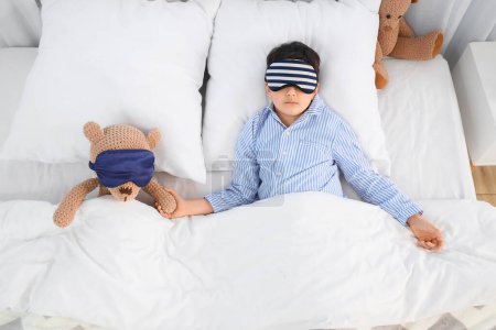 Téléchargez les photos : Petit garçon mignon avec ours en peluche et masques de couchage dans la chambre - en image libre de droit
